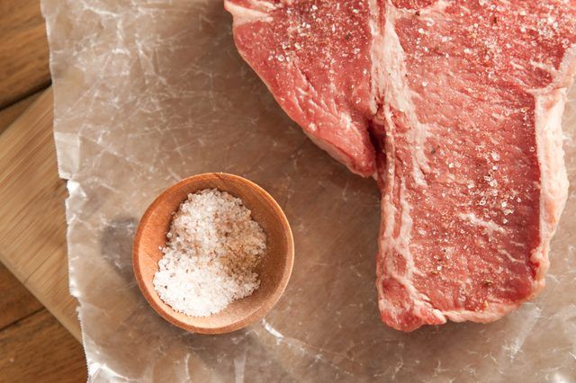 Steak cru à côté d'un petit bol de sel.